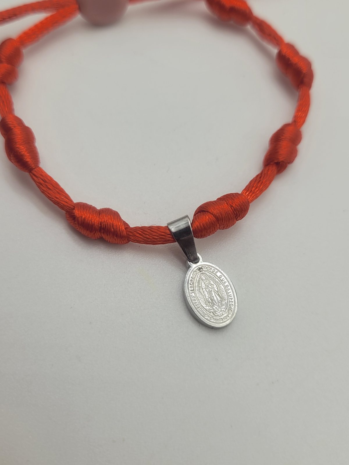 Detalle de pulsera roja de siete nudos con medalla